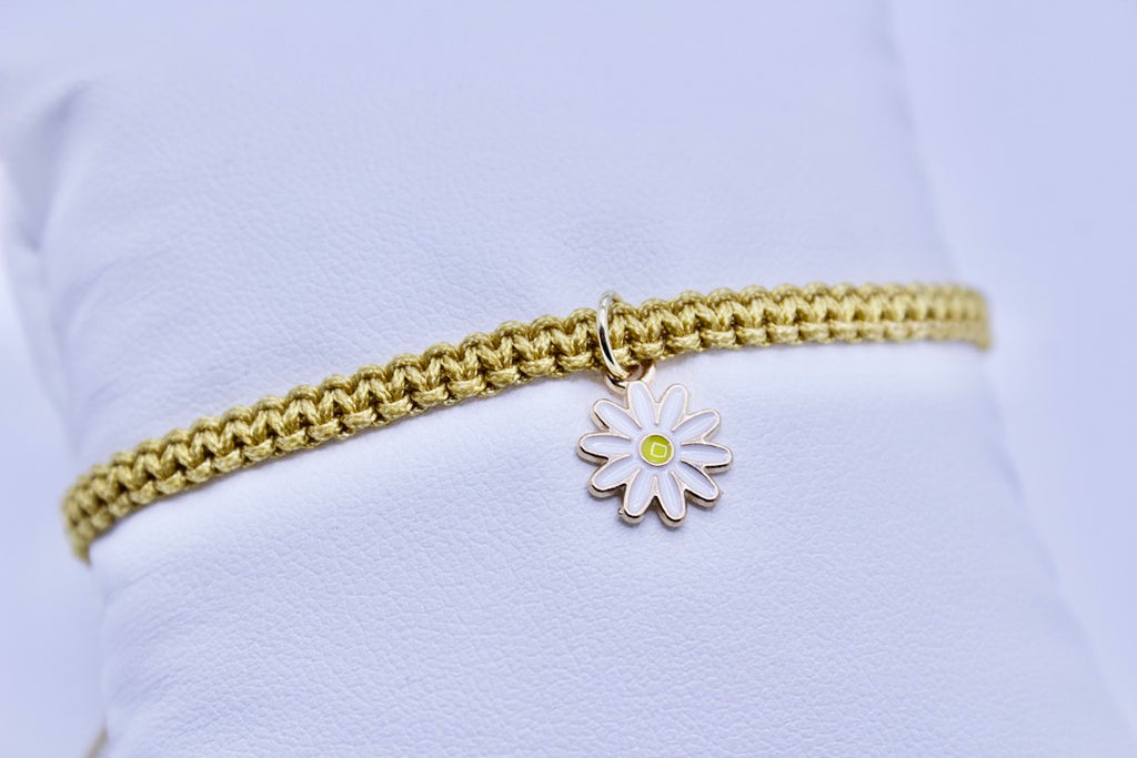 Gold bracelet with a silver daisy charm on a light blue background