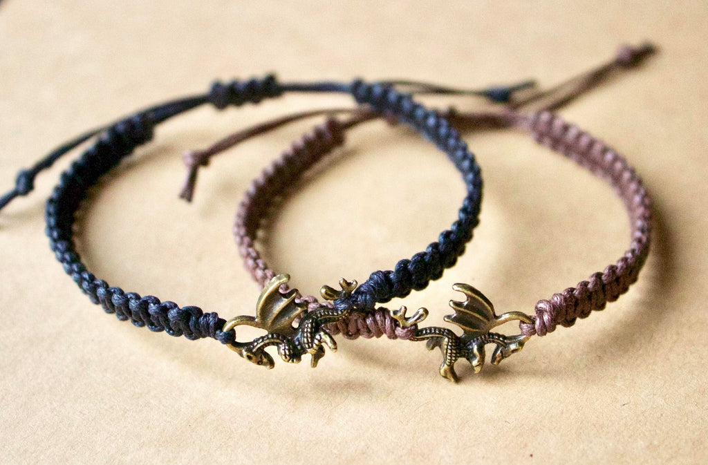 Two braided bracelets with dragon charms on a beige background