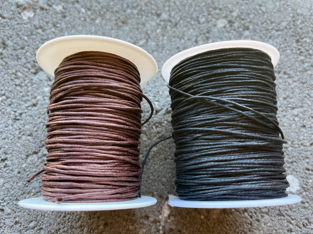 Two spools of thread, one brown and one black, on a textured surface.