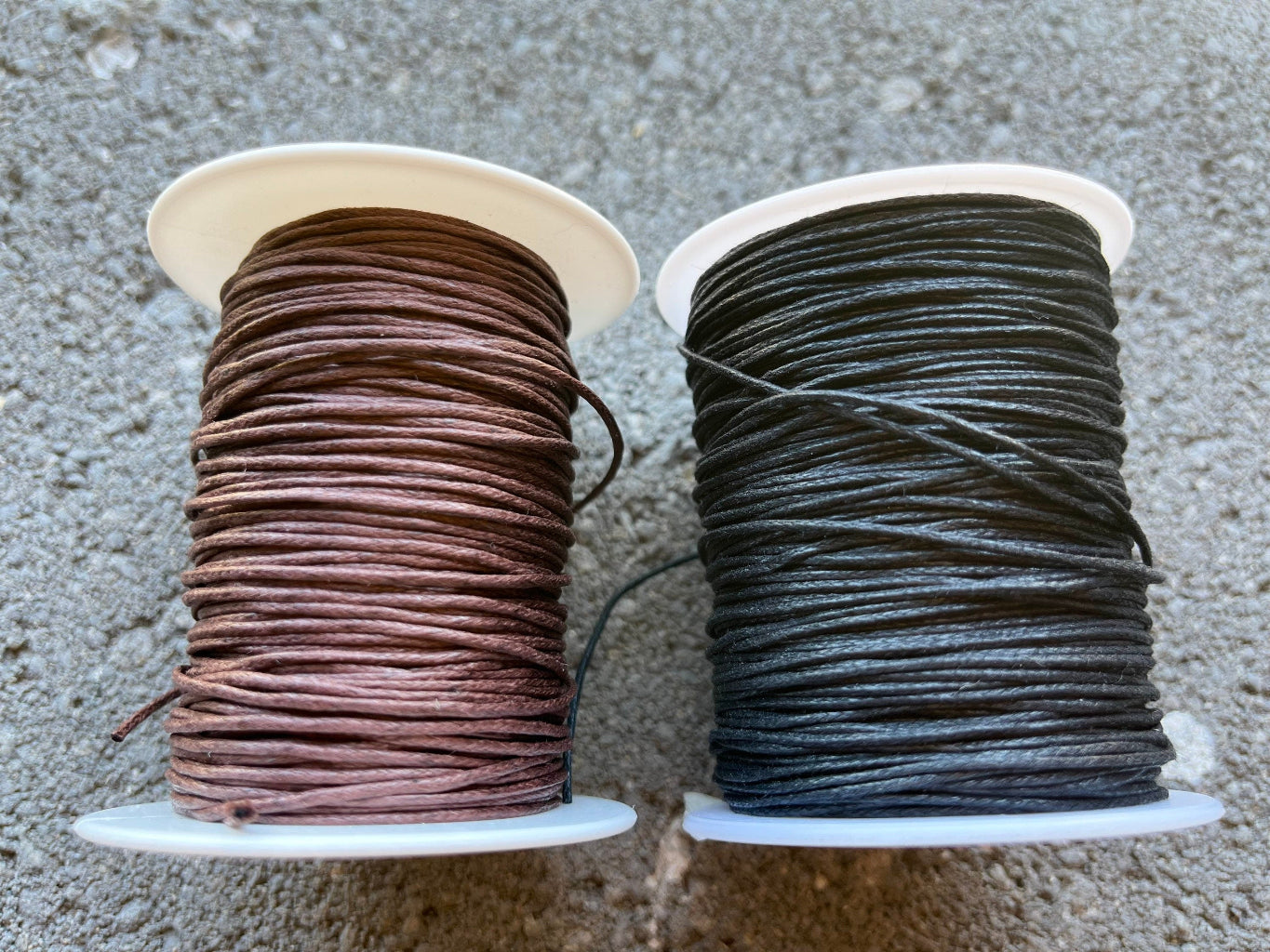 Two spools of thread, one brown and one black, on a textured surface.