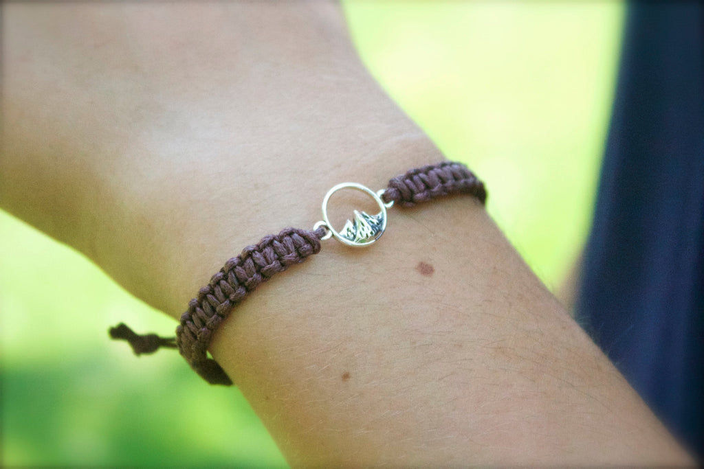 Bracelet with a leaf charm on a wrist against a blurred green background