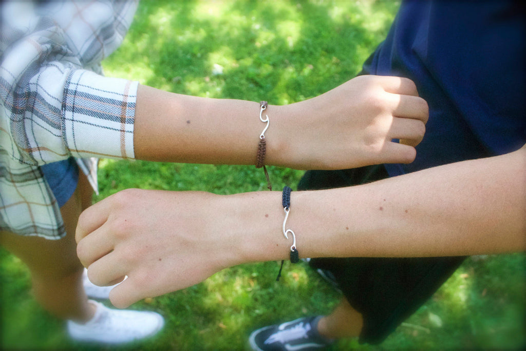Two wrists wearing silver bracelets with a grassy background