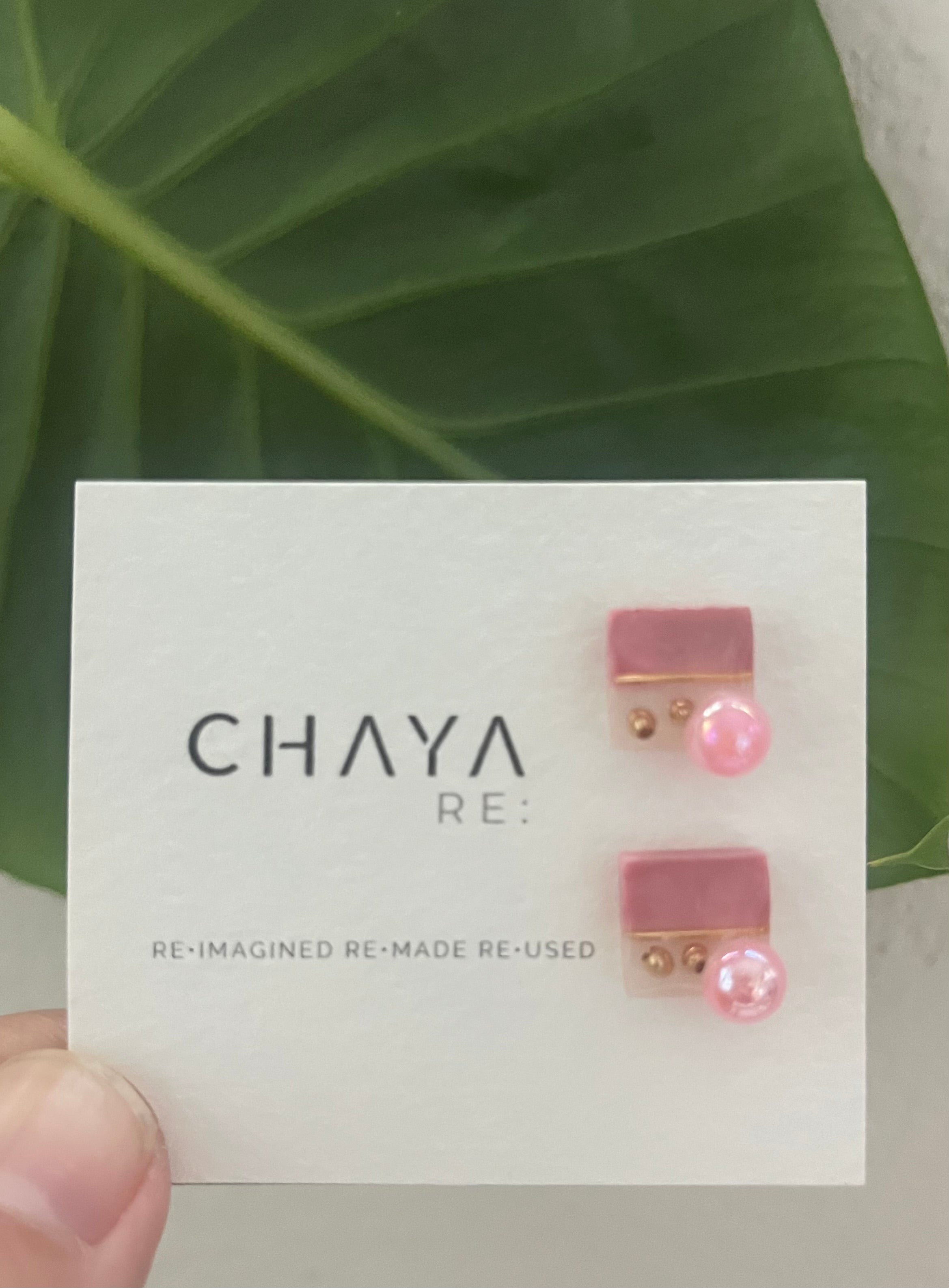 Pink earrings on a Chaya card with green leaves in the background