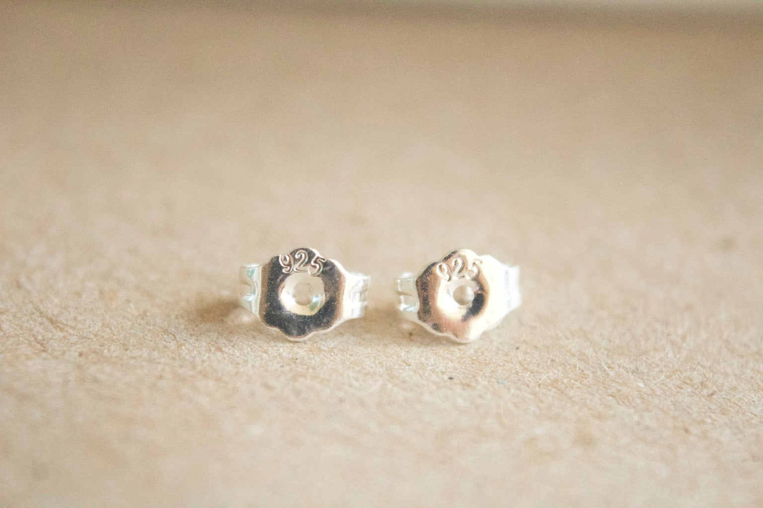Pair of silver paw print earrings on a beige background