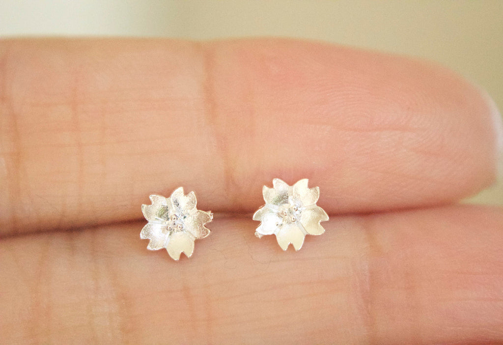 Silver flower-shaped earrings on a person's finger