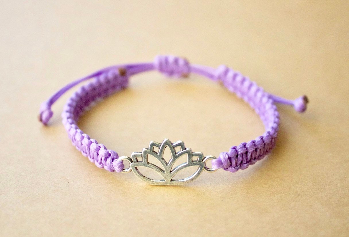 Purple bracelet with a silver lotus flower charm on a beige background