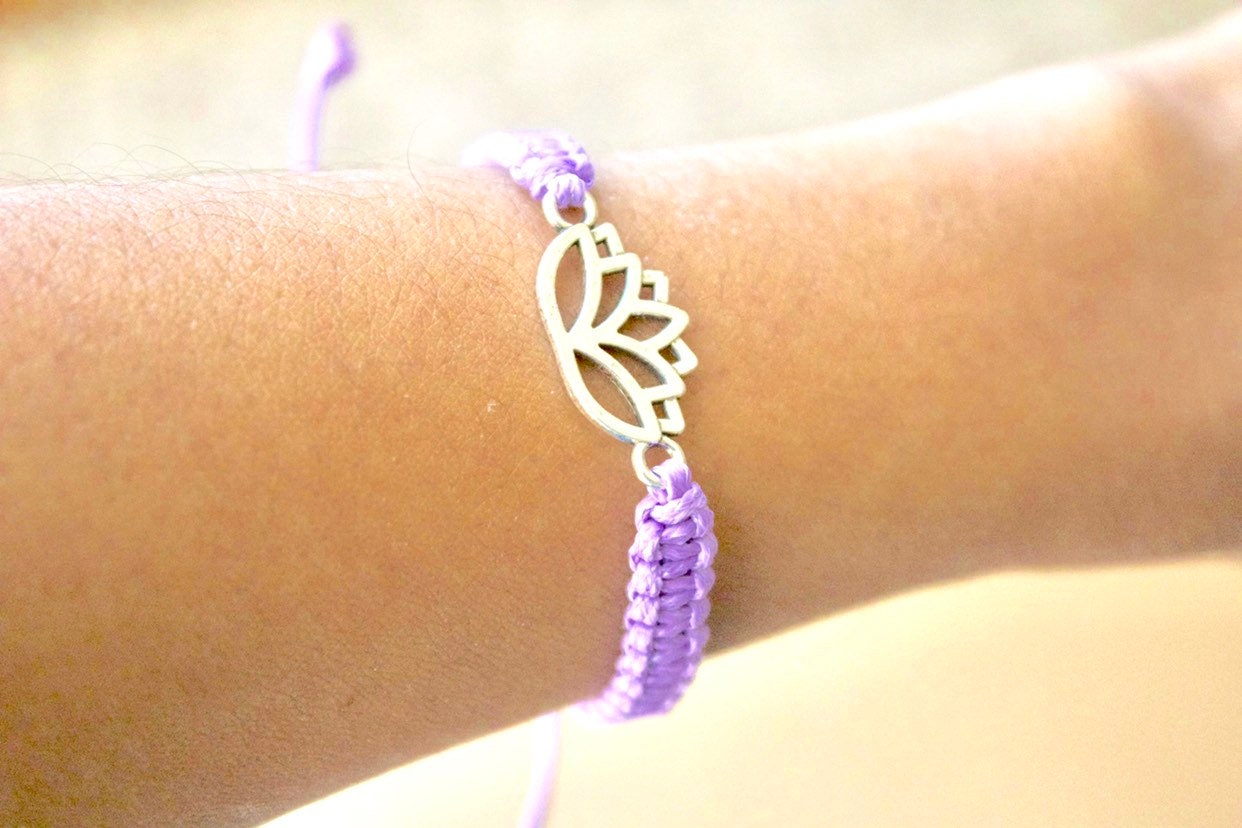 Purple beaded bracelet with a silver leaf charm on a wrist against a blurred background