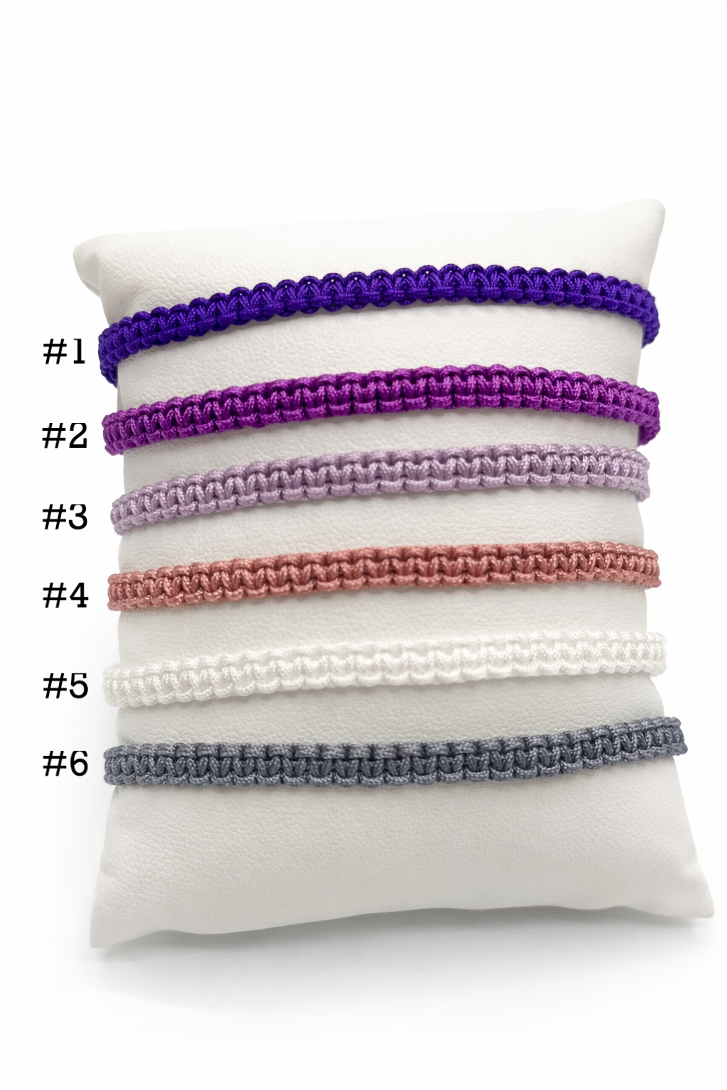 Set of six purple bracelets on a white cushion with numbers indicating their order.