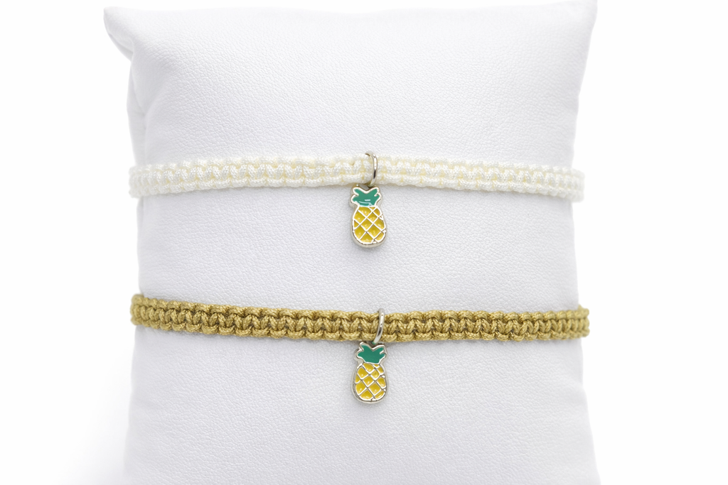 Two bracelets with pineapple charms on a white surface