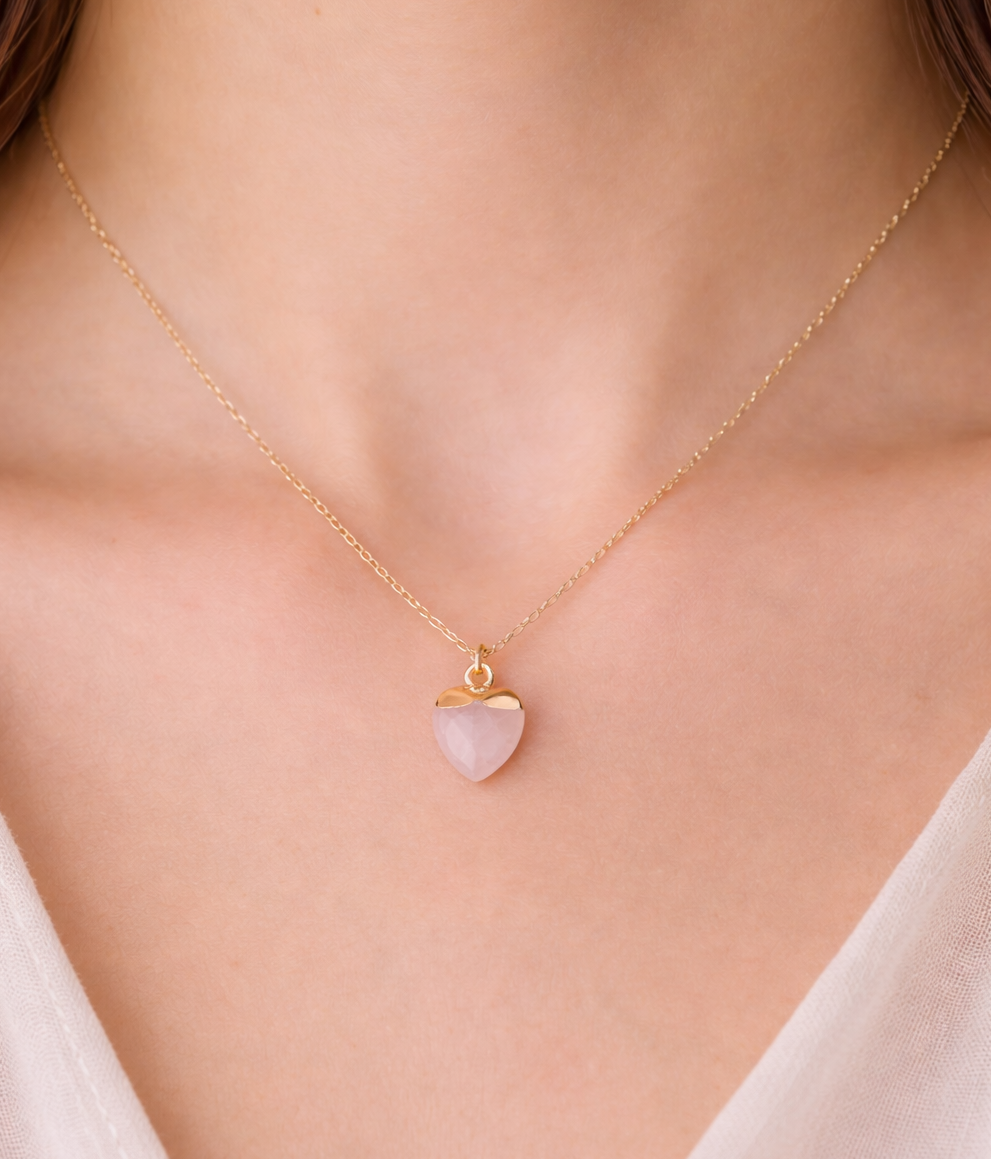 Necklace with a heart-shaped pink pendant on a person wearing a white top.